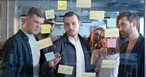 Diverse people of startup project standing in front of board with tasks and to Stock Footage 180043877