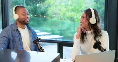 Diverse podcast hosts referencing laptop, gesturing into mics and replying while Stock Footage 342233168