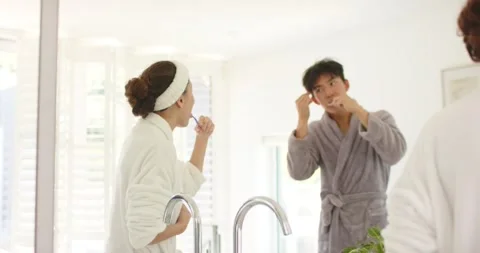 Diverse robe-clad couple doing AM routine she brushing at sink he flossing using Stock Footage 336658478