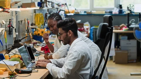 Diverse Robotics Engineers Collaborating on Laptop in Workshop Stock Footage 343506233