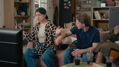 Diverse Roommates Arguing over TV Remote Control on Couch Stock Footage 336623094