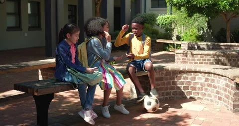 Diverse schoolchildren sitting on bench at school watching boy coming with Stock Footage 345071379