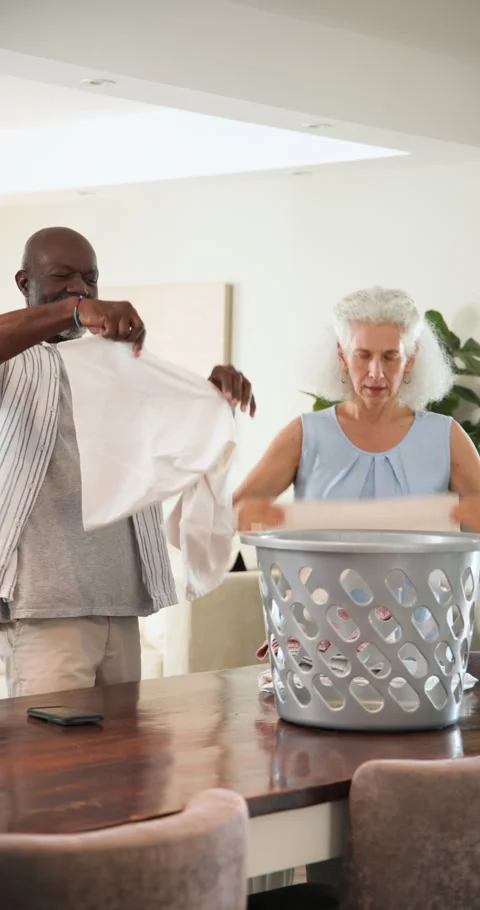 Diverse senior couple folding laundry after unloading basket at table then 스톡 동영상 314025588
