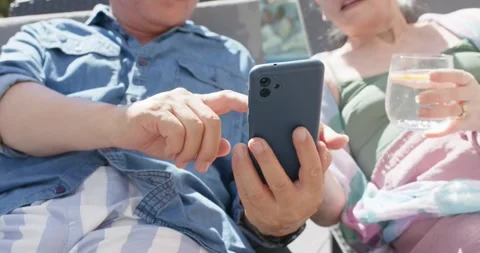 Diverse senior couple resting poolside, man tapping phone showing screen to Stock Footage 336306052