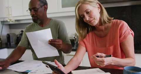 Diverse senior couple using tablet computer paying bills in kitchen Stock Footage 148890096