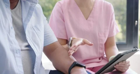 Diverse senior man checking watch as Asian nurse in scrubs tapping tablet Stock Footage 340974810