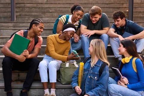 Diverse student group interacting, sharing smartphone on stairs Stock Photos