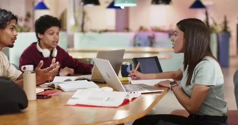 Diverse students around wooden table discussing coursework using laptops after Stock Footage 340987249