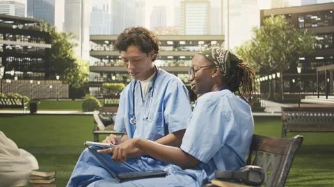 Diverse students in blue scrubs comparing notes on open textbook Stock Photos