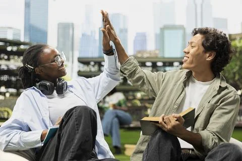 Diverse students celebrating teamwork with high five on outdoor campus lawn Stock Photos