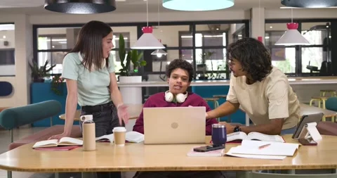 Diverse students leaning in at study table after seated student reacting, Stock Footage 339320822