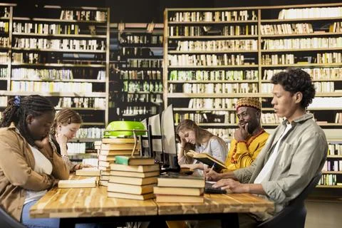 Diverse students learning together in group study session at long library table Stock Photos