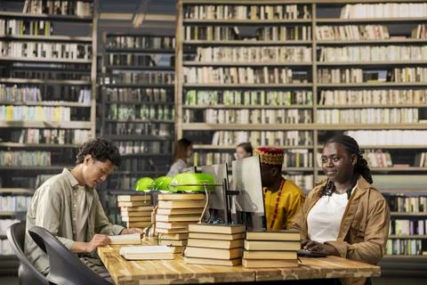 Diverse students learning together in library study group at shared wooden desk Stock Photos