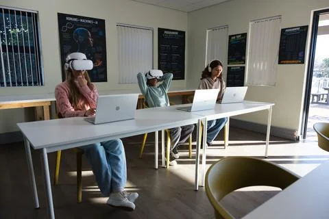 Diverse students sitting at white table in school lab using silver laptops, VR Stock Photos