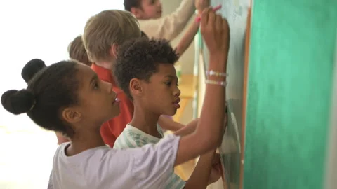 Diverse students writing on chalkboard in classroom Stock Footage 339332281