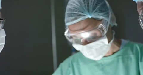 Diverse surgeons with face masks talking during surgery in operating room in Stock Footage 345033598