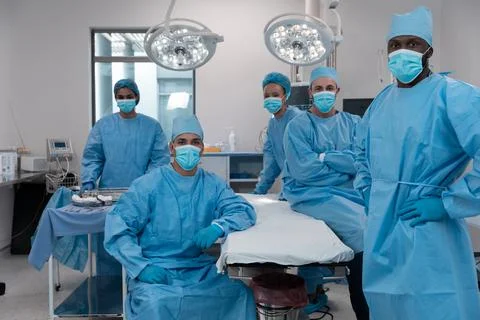 Diverse surgeons wearing face masks and protective clothing in operating theatre Stock Photos