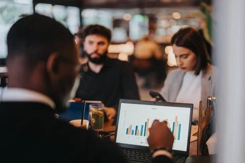 Diverse team analyzing sales data during a business meeting at a cafe Stock Photos