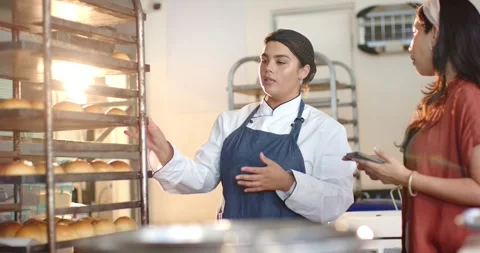Diverse team in bakery, chef white coat pointing to fresh rolls, coworker with Stock Footage 341242119