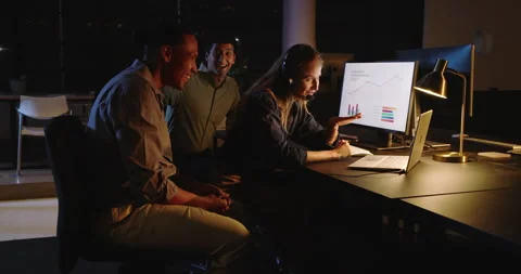 Diverse team collaborating late at night, analyzing data on computer in modern Stock Footage 315966902