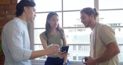 Diverse team leaning on loft ledge, woman showing phone, men holding mugs, Stock Footage 337944672
