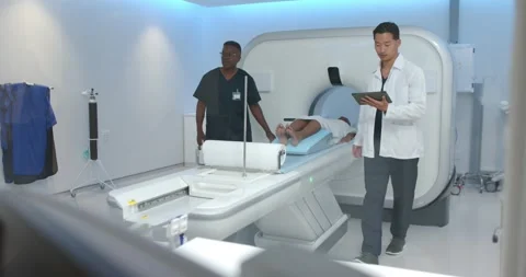 Diverse team moving patient at scanner with blue pad while clinician starting Stock Footage 344326362