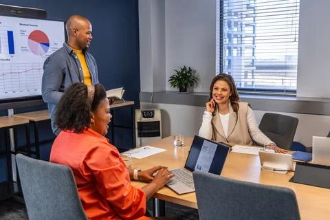 Diverse team presenting pie chart laptops conference table woman in beige vest Stock Photos