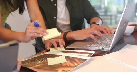 Diverse team reviewing prints at table, writing sticky notes, pointing at Stock Footage 335895825