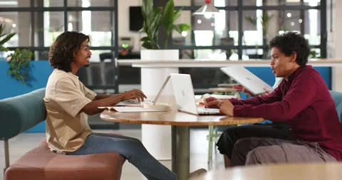 Diverse team at round table, left typing on laptop, right lifting blue notebook Stock Footage 340069896