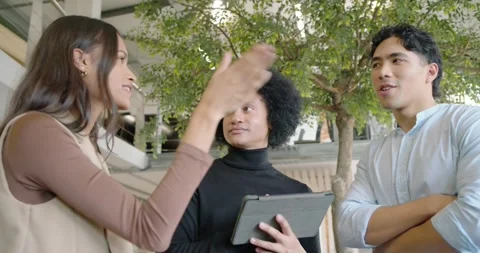Diverse team starting project talk in atrium presenter in black using tablet Stock Footage 337944563