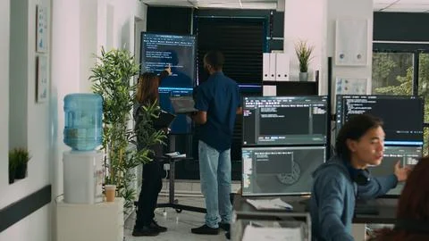 Diverse team of system developers analyzing code on big tv screen Stock Photos