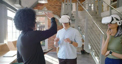 Diverse team trainer holding tablet starting VR demo in loft guiding two in Stock Footage 337944595