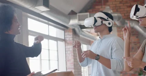 Diverse team using white VR headsets in loft, trainer entering left with tablet Stock Footage 339961399