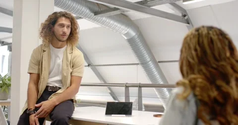 Diverse team watching man sitting on desk in office explaining after colleague 스톡 동영상 341079632