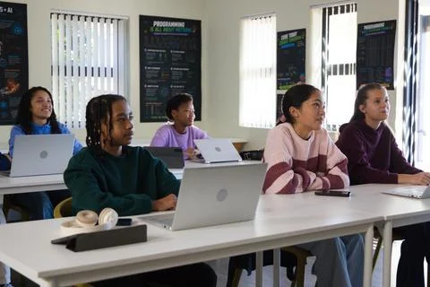 Diverse teenage students coding on silver laptops in coding lab with headphones Stock Photos