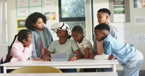 Diverse teens gathering in class watching African teen putting on VR headset and Stock Footage 340393277