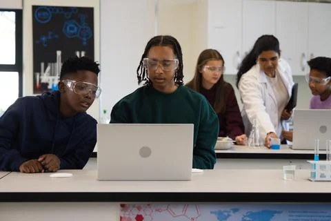 Diverse teens using laptop wearing goggles in science lab, instructor in lab Stock Photos