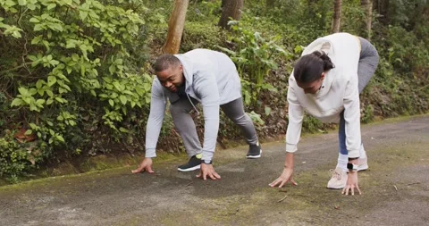 Diverse training duo crouching at sprint start on path wearing running shoes Stock Footage 344339657