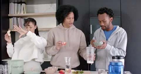 Diverse trio making drink peeling banana scooping cream adding fruit into Stock-Footage 345607654