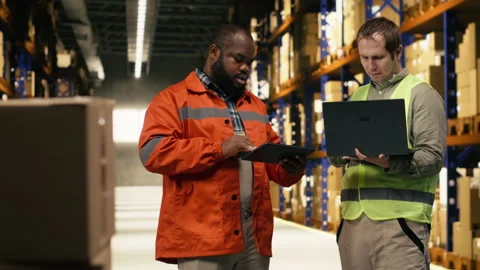 Diverse warehouse team, update parcel tracking software, with laptop and tablet Stock Footage 332909442