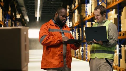 Diverse warehouse team, update parcel tracking software, with laptop and tablet Stock Photos