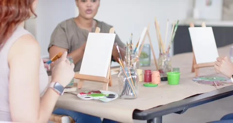 Diverse women checking brushes, dipping brush, readying canvas while camera Stock Footage 337286407