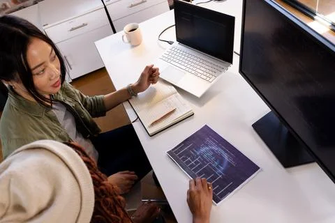 Diverse women collaborating on coding project at office desk with laptop and 库存照片