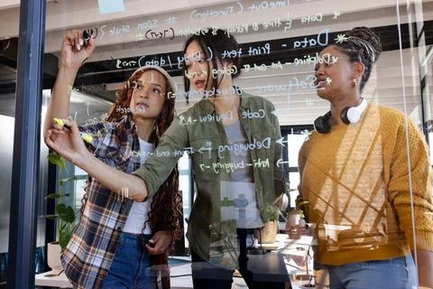 Diverse women collaborating on coding project, writing on glass board in modern Foto stock