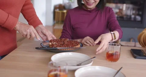 Diverse women at dining table, orange host cutting tart on blue-pan, senior in Stock Footage 339267820