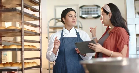 Diverse women manager tapping tablet cueing chef in coat pointing at rack Stock Footage 335514822