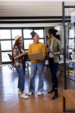 Diverse women in office collaborating on coding project with laptops, smiling Stock Photos