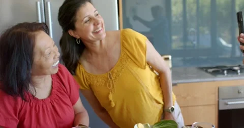Diverse women posing at kitchen island with egg bowls as friend lifting phone Stock Footage 335928048