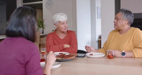 Diverse women sitting at dining table, right woman stirring and talking, senior Stock Footage 339267835