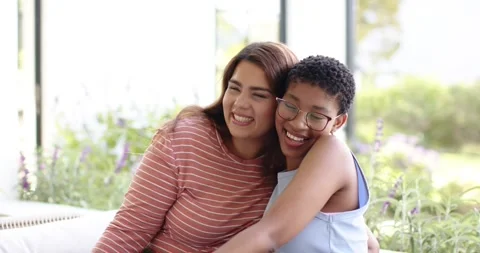 Diverse women sitting on sofa by window, right woman putting arm, cuddling with Stock Footage 340257241